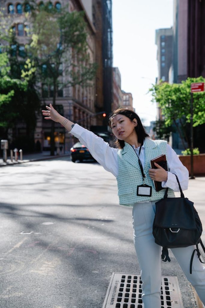 Businesswoman with a bag hailing a taxi in a vibrant city street on a sunny day.