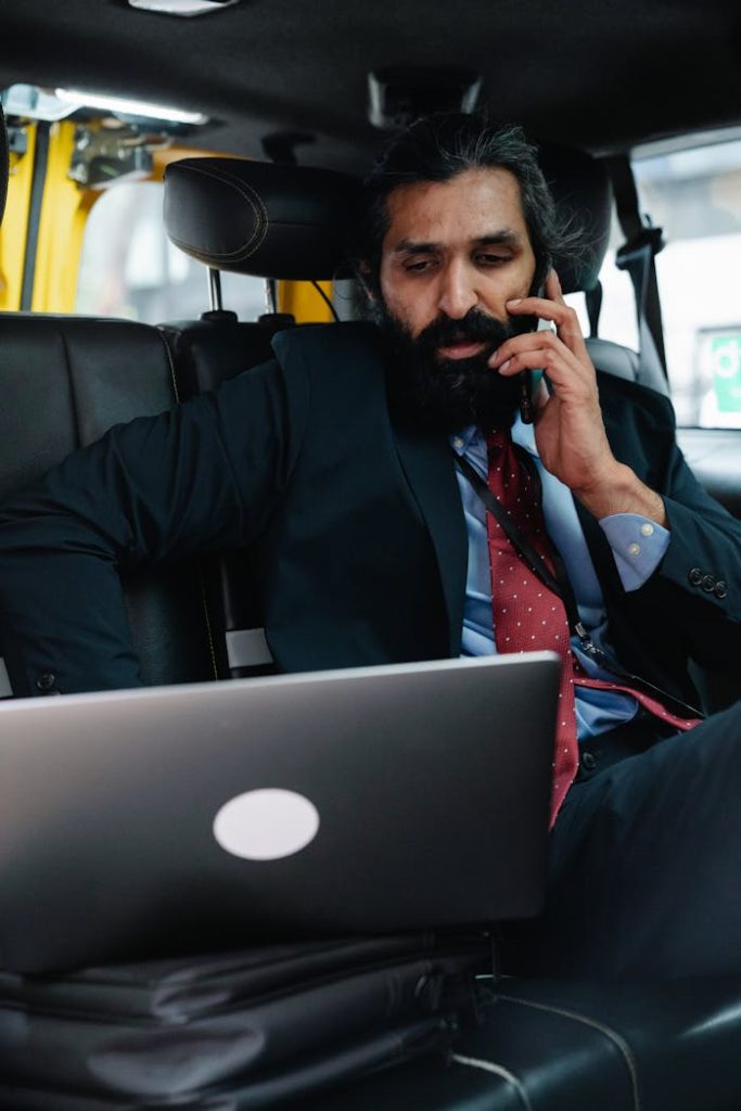 Professional man in a taxi working on laptop and talking on phone.